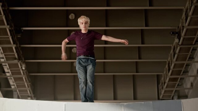 Caucasian teenager with blonde hair performing street dance under concrete bridge, jumping and executing hip hop moves. Footage is perfect for youth lifestyle brands and urban culture marketing