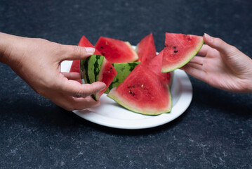 Two hands reach for triangular slices of juicy watermelon on white plate, evoking summer, sharing, freshness and casual kitchen moments. Juicy red watermelon on a plate, healthy food © Мар'ян Філь