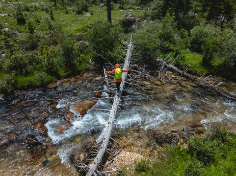 Woman hiker walking on balance at one log bridge across the high altitude mountain stream, crossing the river.