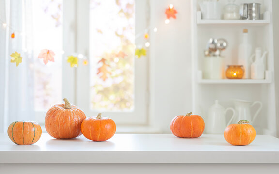 Fresh pumpkins arranged on white table with blurred decorated for holiday kitchen interior background