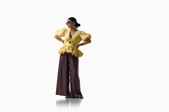 Stylish woman poses in yellow peplum blouse and wide brown trousers. Concept of color styling, statement fashion, feminine silhouette and creative wardrobe.