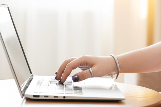 Hand tapping keyboard of laptop computer on table over blurred interior background