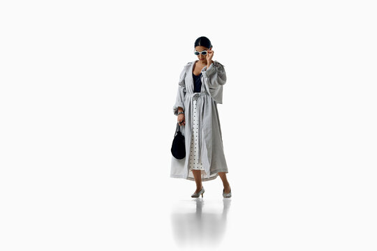 Woman models long gray coat with patterned dress full-body isolated. Concept of layered fashion, elegant personal style, transitional clothing and wardrobe inspiration.
