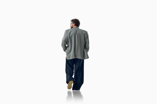 Fashionable man shows back view of gray blazer and wide trousers. Concept of garment design, contemporary tailoring, menswear details and professional wardrobe.
