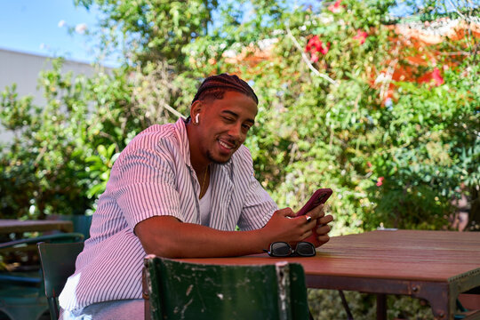 Young man using smartphone and wireless earbuds outdoors