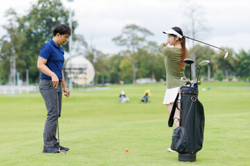 Fototapeta premium Coach teaching woman golf swing technique at driving range, male trainer giving individual instruction during golf lesson, female trainee practicing outdoor sport