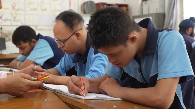Young students with down syndrome concentrating on their studies during a lesson in a classroom, with a teacher helping one of them learn to write, showcasing special education and inclusion