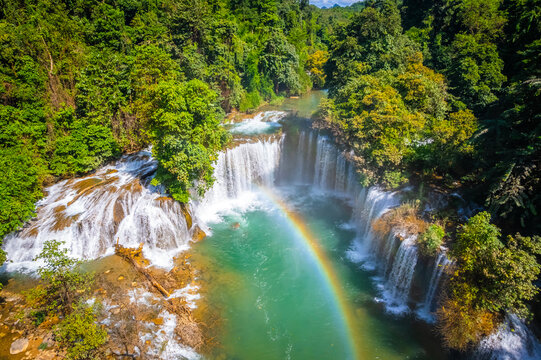 Aerial view of vibrant rainbow over turquoise river pool with waterfall cascading in lush green forest at Glue-Thor Waterfall (Kyone Htaw Waterfall), Kayin State, Myanmar.