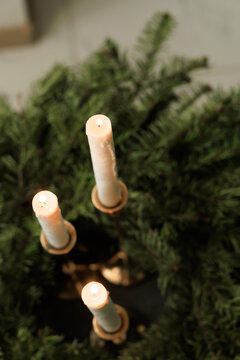 Three candles lit on a wreath displayed indoors with greenery