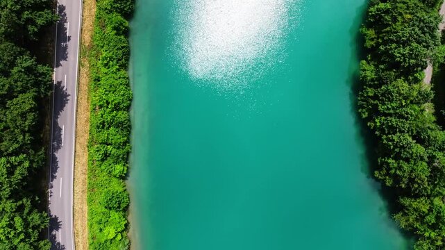 Mavic 3 Pro drone top down view flying slowly over the turquoise Soca river in Slovenia. Aerial birdseye perspective of a scenic road running along the beautiful blue green alpine water valley.
