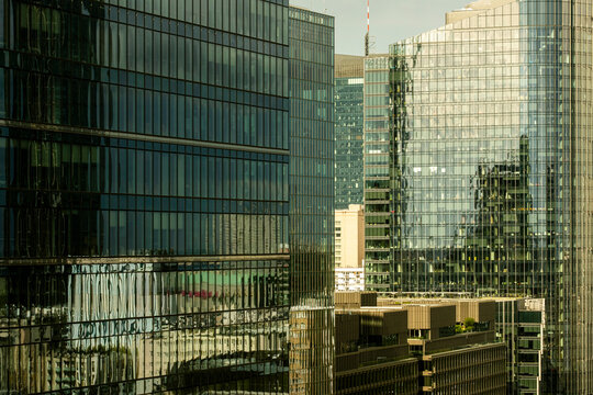 Reflective glass towers in Warsaw Poland form layered facades and dense urban reflections across a modern city scene with repeated vertical grids and warm light
