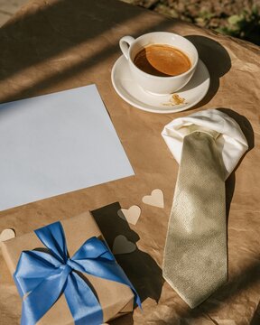 Patterned necktie and coffee cup on a mocha brown surface with a gift box and copy space for Father's Day greeting layouts