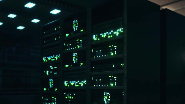 Several server racks are lit up with green lights in a data center at night. The space is primarily dark except for the lights from the servers and some equipment.