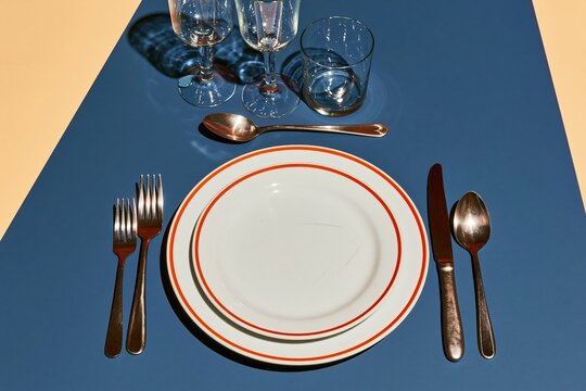 Formal place setting with red rimmed plates on a blue tabletop, featuring polished cutlery and glassware for dining etiquette and tableware catalogs