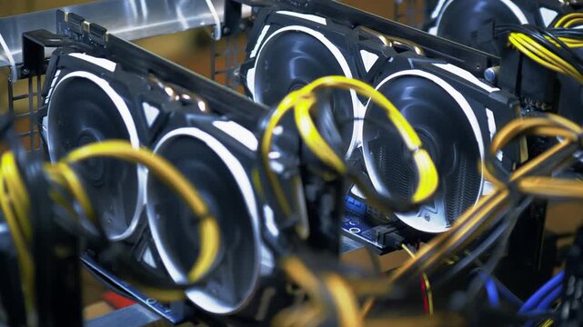 Open GPU mining rig packed with several graphics cards is seen from above as dual cooling fans spin beneath looping yellow power cables