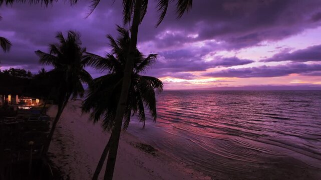 Timelapse style view of purple sunset clouds over a tropical beach and calm sea.