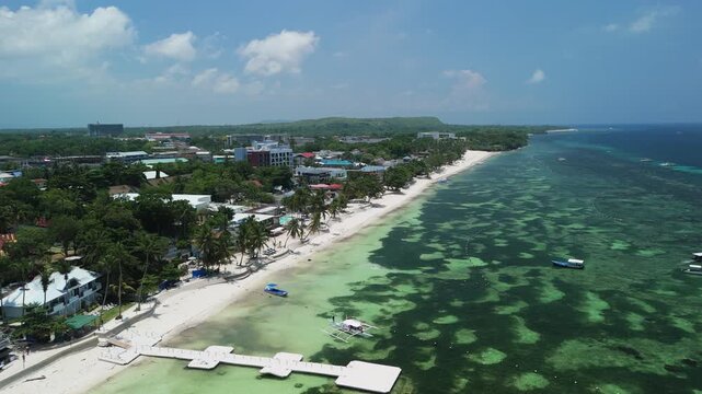 Drone flies over and orbits right above Alona Beach, revealing white sand, shallow turquoise water, boats, and the Panglao coastline