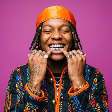 Stylish Black man with silver grillz and orange durag. Hip hop artist smiling on purple background. Urban fashion portrait.