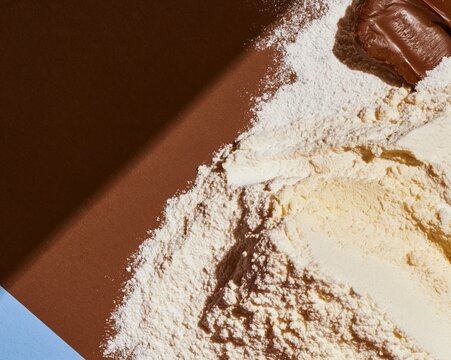 White flour and icing sugar drifts on a dark cocoa brown surface, featuring a tactile powdery texture for food packaging and layout backgrounds