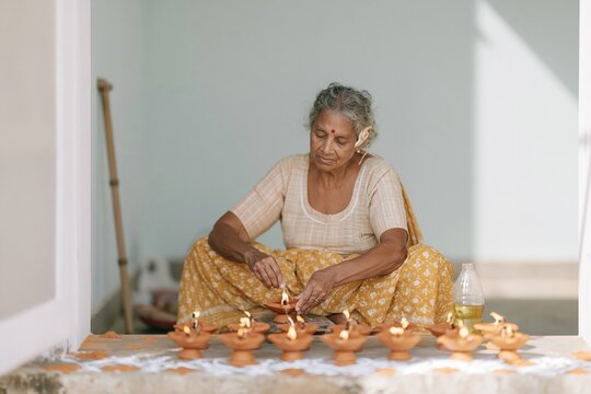 Senior Indian woman preparing terracotta oil lamps on a tiled porch, a calm and capable scene for festival preparation and aging