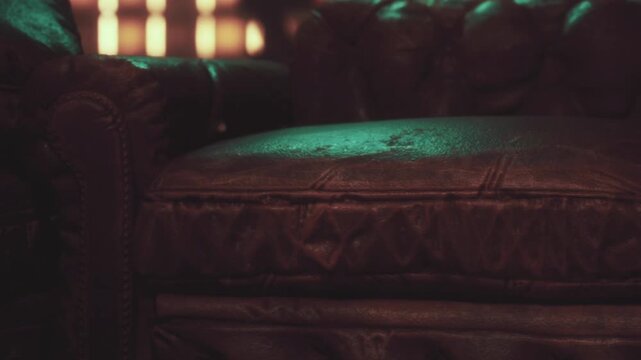 A leather couch sits in a dark room. There is a green light reflecting off the surface. The atmosphere feels cozy and inviting, making it a good spot for sitting and relaxing.