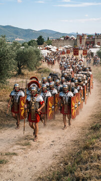 Una legi&oacute;n de soldados romanos con armadura, escudos y estandartes marcha en formaci&oacute;n por un camino de tierra junto a un fuerte de madera.