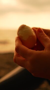 Egg peeling sunset hands preparing a hardboiled snack on a beach during a peaceful golden hour