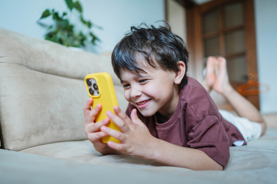 Smiling boy lying on sofa playing with phone at home