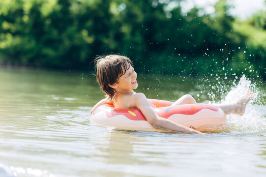 A smiling boy in an inflatable ring splashes water in a lake