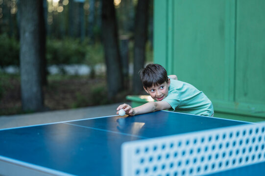 Boy reaching for a ball while playing table tennis outdoors