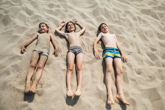 Boys sunbathe on the sand at the beach during summer