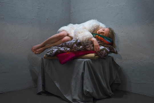 A woman sleeps on a stack of cushions in a grey room