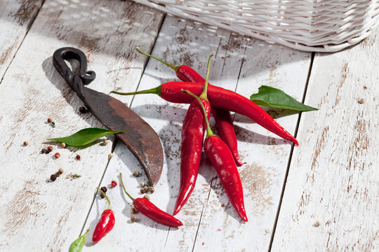Red chili peppers (Capsicum) and an old knife on white wooden table, studio shot