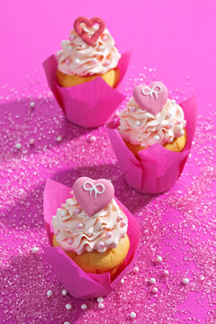 Three cup cakes in pink wraps on pink ground