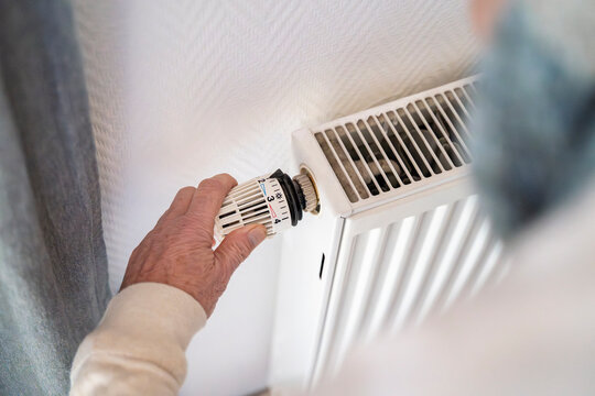 Detail of hand adjusting radiator thermostat indoors for energy saving
