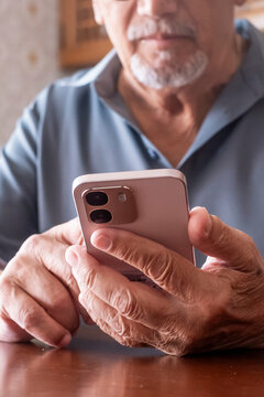 Senior man with wrinkled hands holding a modern smartphone, connecting with digital technology and demonstrating older generations embracing mobile communication and internet usage