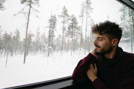 Man looks out cabin window at snowy winter landscape in Finland