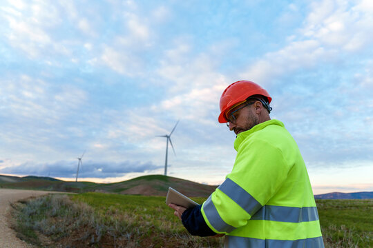 Engineer inspecting wind turbine with digital tablet outdoors