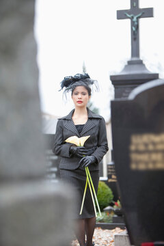 Germany, Bavaria, Young woman with flower at graveyard
