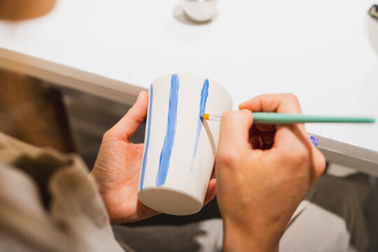 Woman paints blue stripes on a ceramic cup in a workshop
