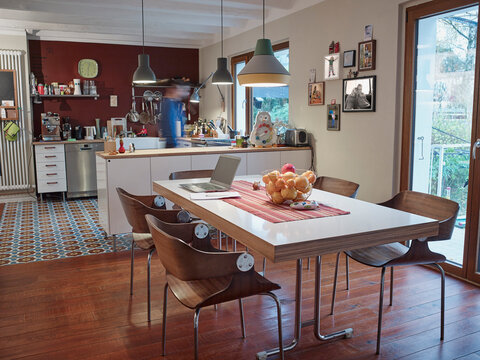 Laptop on dining table in open plan kitchen with man in background