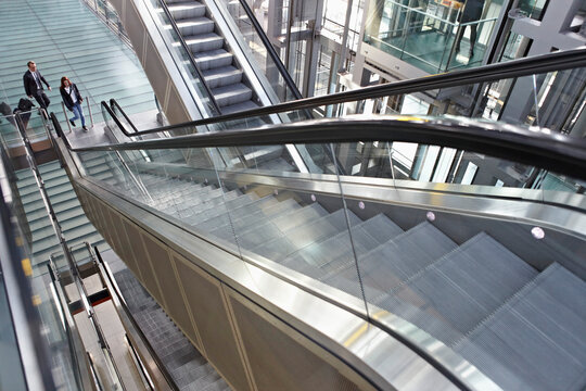 Germany, Cologne, Young woman and mature man moving up escalator at airport