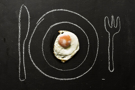 Fried egg on chalkboard with painted table setting, close up
