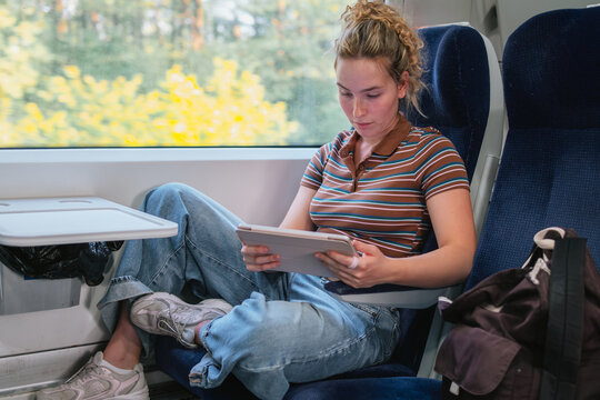 Woman uses a tablet while sitting by the window on a train