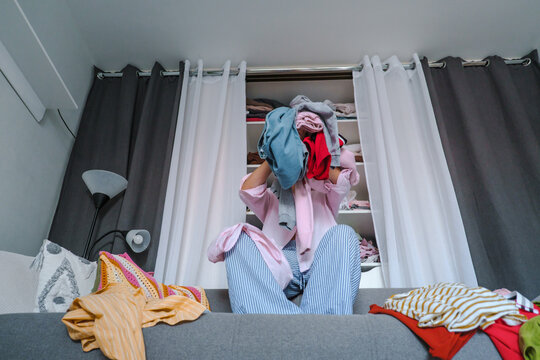 Woman holding pile of clothes over face during wardrobe declutter