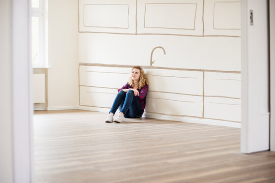 Young woman in new home sitting on floor thinking about interior design