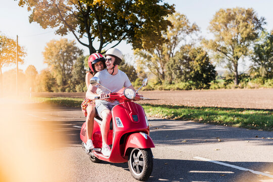 Happy young couple riding motor scooter on country road