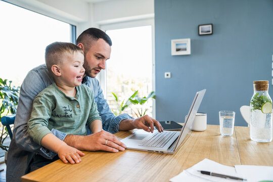 Smiling father and son use a laptop together at home