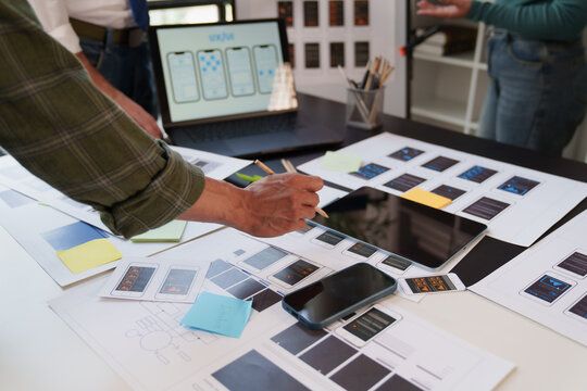 UX UI designers collaborating on mobile application wireframes and user experience layouts, planning and creating website interface development on a workspace desk