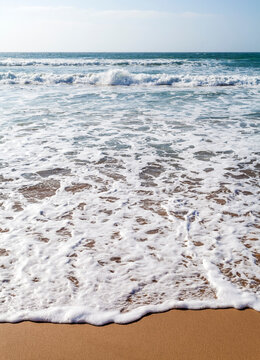 Ocean waves crash onto the sandy shore of Praia do Amado